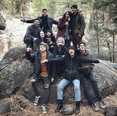 a group of people sitting on top of a large rock in the middle of a forest