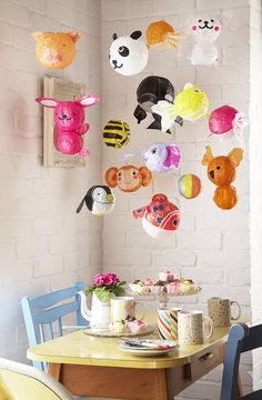 a dining room table and chairs with colorful decorations on the wall above it, along with an assortment of stuffed animals hanging from the ceiling