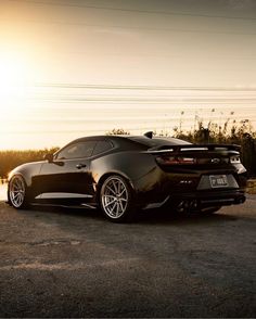 the rear end of a black sports car parked in front of a body of water