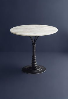 a white marble table with black metal base on a dark blue background in front of a gray wall