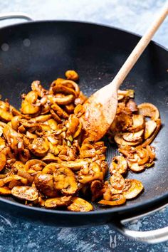 mushrooms being cooked in a skillet with a wooden spoon
