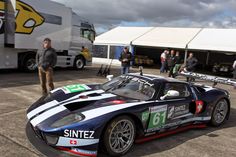 a race car is parked in front of some people on the tarmac with other cars behind it