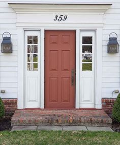a red front door with two sidelights and brick steps in front of a white house