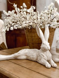 a white rabbit figurine sitting on top of a table next to a basket filled with flowers