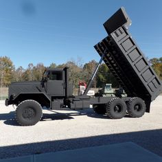 a large black dump truck parked on top of a parking lot next to a forest