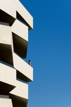 a person standing on top of a tall white building next to a blue cloudless sky