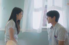 a young man and woman standing next to each other in front of a curtained window