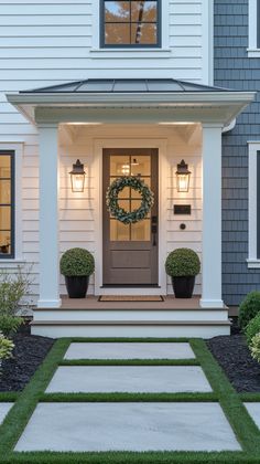 the front door of a white house with two planters and a wreath on it