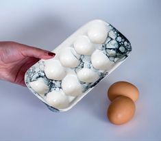 a hand holding a container filled with white and brown eggs next to an egg shell