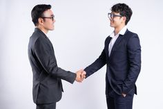 two men in suits shaking hands while standing next to each other on a white background