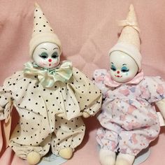 two small dolls sitting next to each other on a pink surface with polka dot fabric