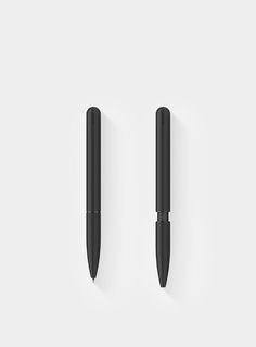 two black pens sitting next to each other on top of a white surface with one pen in the middle