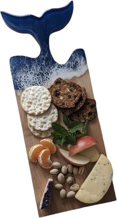 a wooden cutting board topped with cheese, crackers and fruit next to a whale tail