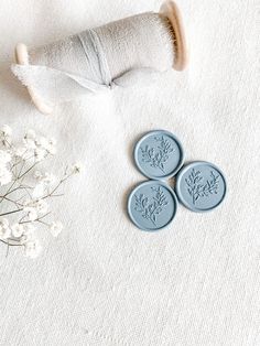 three blue buttons sitting on top of a white cloth next to a spool of thread