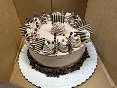 a cake with white frosting and chocolate decorations in a cardboard box on top of a table