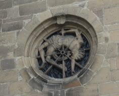 a circular window on the side of a building with a statue of a man holding a wheel