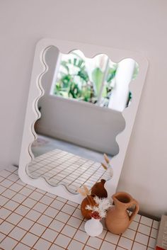 a mirror sitting on top of a counter next to a vase and potted plant