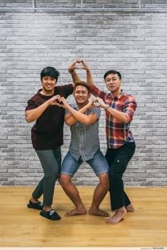 three young men standing in front of a brick wall posing for the camera with their arms around each other