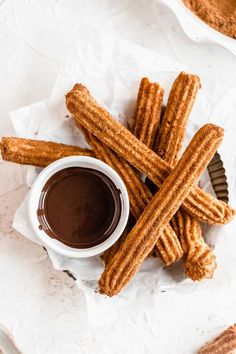 churro sticks with dipping sauce in a white bowl on top of some parchment paper