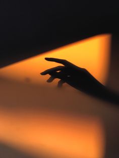 a person's hand reaching for something in the air with orange light behind them
