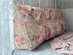 a pink flowered pillow sitting on top of a bed next to a white headboard