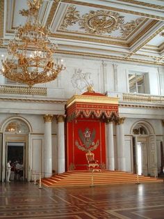 an ornately decorated room with red and gold furniture, chandelier and stairs