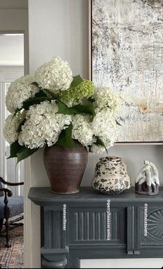 a vase filled with white flowers sitting on top of a table next to a painting