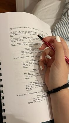 a woman is writing on a book with a pencil in her hand while holding a pen