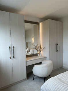 a white bed sitting under a large mirror next to a closet filled with drawers and cupboards