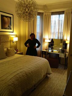 a woman standing in a bedroom next to a bed with a chandelier hanging from the ceiling
