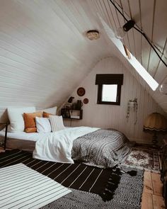 an attic bedroom with white walls and black and white rugs on the floor next to bed