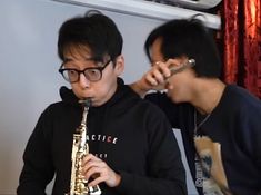 two young men are playing the saxophone in front of each other and one is wearing glasses