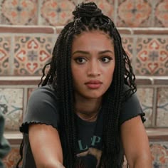 a woman with long braids sitting on the ground in front of some tile walls