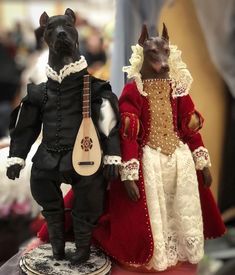 two figurines of dogs dressed in period clothing, one holding a ukulele