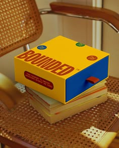 a stack of books sitting on top of a wooden chair next to a yellow box