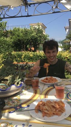 a man sitting at an outdoor table with food in front of him and smiling for the camera