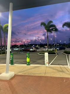 an empty parking lot at dusk with palm trees in the background and cars parked on the street