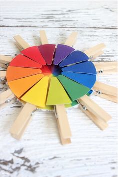 a rainbow colored wheel with wooden sticks sticking out of it on a white wood background