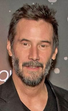 a close up of a person wearing a black shirt and suit with a gray beard