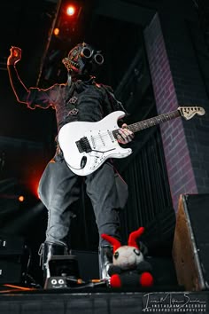 a man in gas mask playing an electric guitar on stage with a stuffed animal behind him