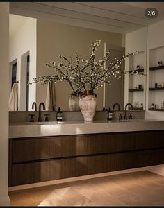 a bathroom with two sinks and a large vase filled with flowers on top of it