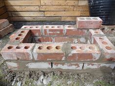 a brick fire pit sitting in the middle of a yard next to a pile of bricks