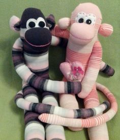 two stuffed animals sitting next to each other on a green surface and one is holding a pink heart