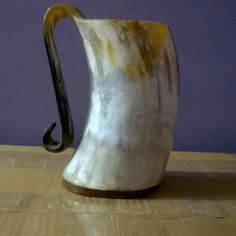 a white and brown vase sitting on top of a wooden table next to a purple wall