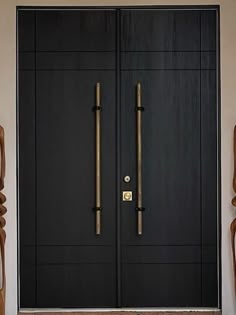 two wooden chairs sitting next to each other in front of a black door with gold handles