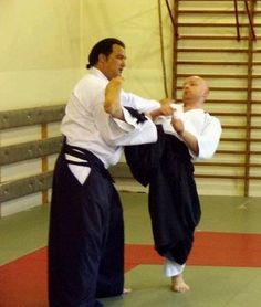 two men in black and white kimonos standing on a red mat with their hands together