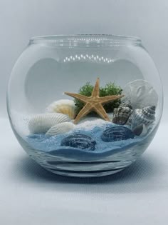 a fish bowl filled with sand and sea shells on top of a white table next to a starfish