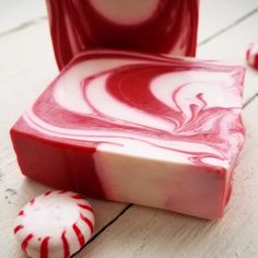 a red and white swirled soap bar next to a peppermint candy cane on a wooden table