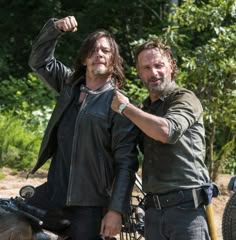 two men standing next to each other on a dirt road