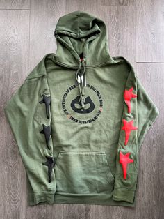 a green hoodie with red and black stars on the sleeves, sitting on a wooden floor